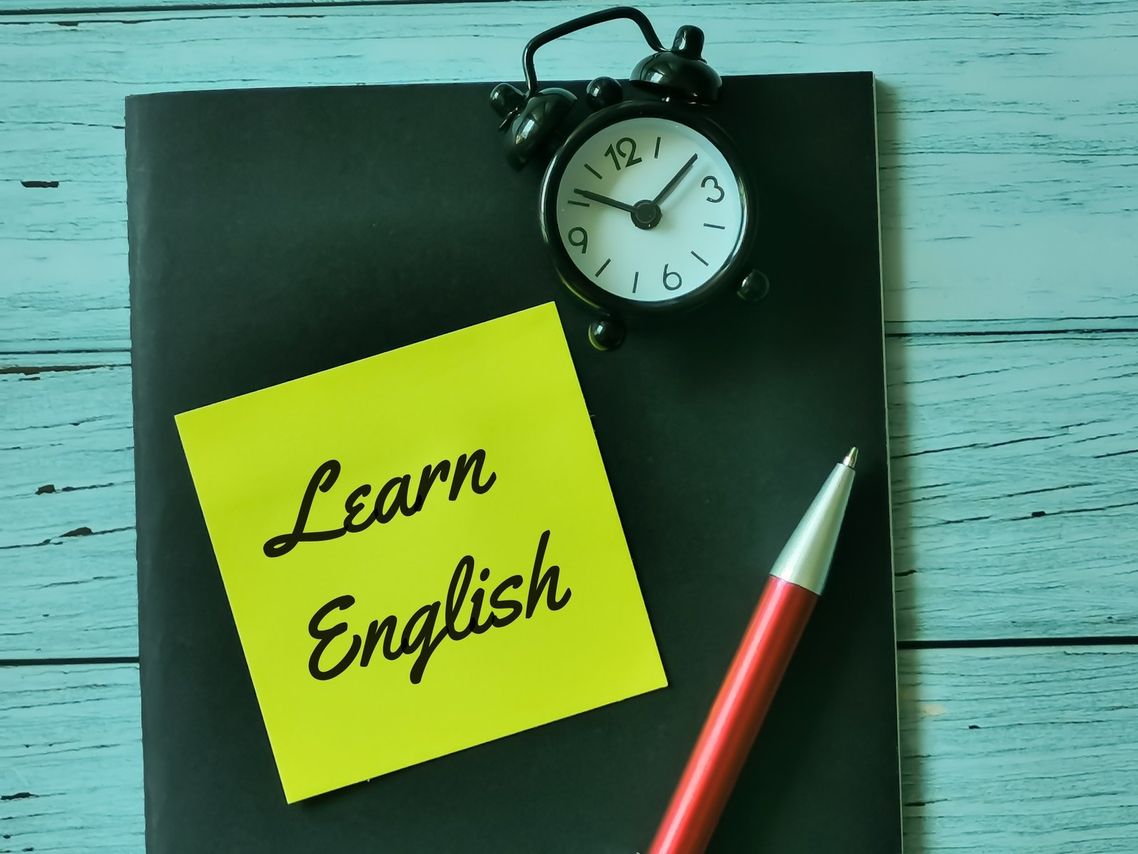 Phrase learn English written on sticky note with a pen,alarm clock and book.